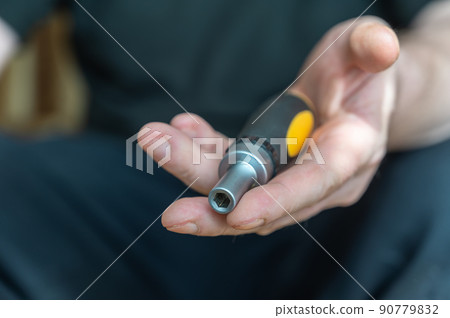The hand of a mature man holding a screwdriver. Hand tool with interchangeable bits. 90779832
