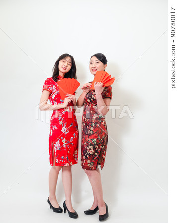 Young asian young and older women in traditional cheongsam holding stacks of red envelopes each in front of white background, symbolizing wealth Young asian young and older women in traditional cheongsam holding stacks of red envelopes each in front of white background, symbolizing wealth 90780017