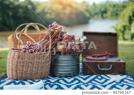 picnic set in the park near river, dried flowers, baskets wine bottle, book and retro gramophone vinyl record. Summer, spring and vacation concept picnic set in the park near river, dried flowers, baskets wine bottle, book and retro gramophone vinyl record. Summer, spring and vacation concept 90780167