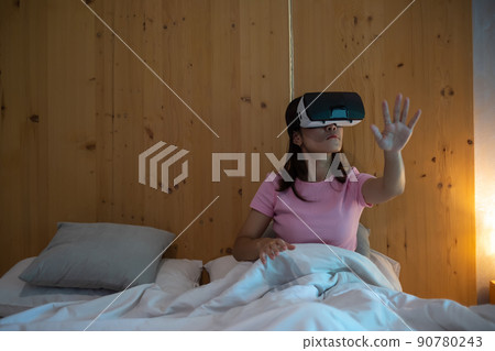 Young woman using virtual reality headset in bed. VR, Future digital technology, game, movies entertainment, metaverse, NFT and 3D cyberspace concept 90780243