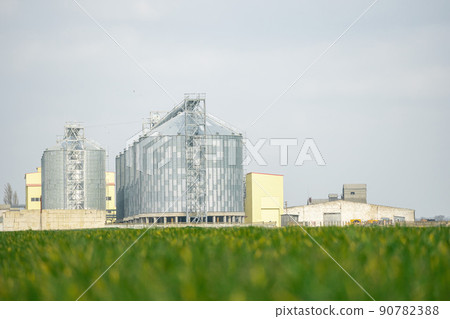 Grain elevator. Metal grain elevator in agricultural zone. Agriculture storage for harvest. Grain elevators on green nature background. Exterior of agricultural factory. Nobody. 90782388