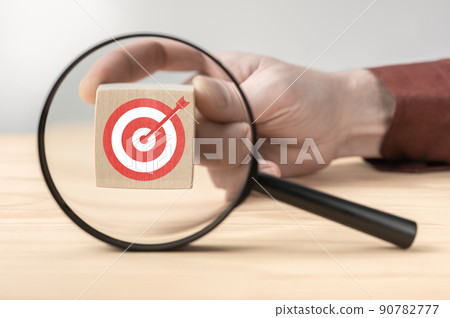 Target board inside of magnifier glass for focus business objective on white background and copy space. Hand hold wooden cube behind magnifying glass. Magnifying glass and target 90782777