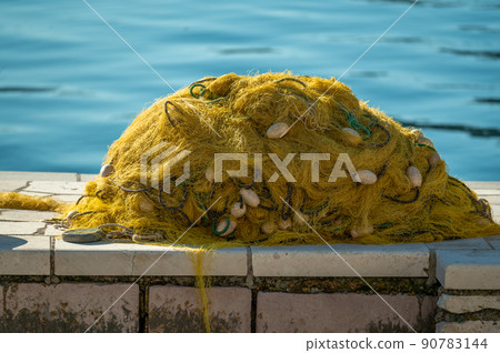 fishing nets. rustic fishing net with buoys and ropes. fishing nets dry on shore. Stacked yellow coloured fishing nets 90783144