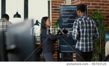 Team of coders analyzing code on wall screen tv comparing errors using digital tablet next to programer working with neural network. Software engineers collaborating on coding group project. Team of coders analyzing code on wall screen tv comparing errors using digital tablet next to programer working with neural network. Software engineers collaborating on coding group project. 90783526