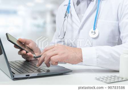 Doctor typing on laptop computer while sitting at the glass desk in hospital office. doctor working in clinic. Doctor is with phone and checking medical records Doctor typing on laptop computer while sitting at the glass desk in hospital office. doctor working in clinic. Doctor is with phone and checking medical records 90783586