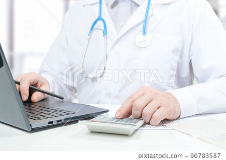 Doctor working with medical statistics and financial reports. doctor counts on calculator and enters data into laptop. male doctor using laptop and calculator at office 90783587
