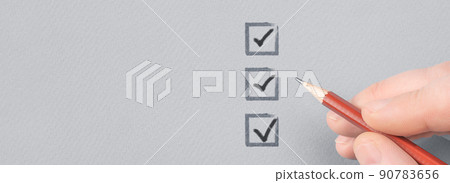 hand with pencil writing check mark on Checklist. Cropped Hand Marking On Check Box on Gray paper. Completed tasks are ticked off on a to-do list 90783656