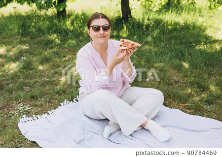 Funny brunette girl in sunglasses eating pizza on nature background. Attractive girl feels hungry and loves the taste. Entire pizza for myself. Fast food banner 90784469