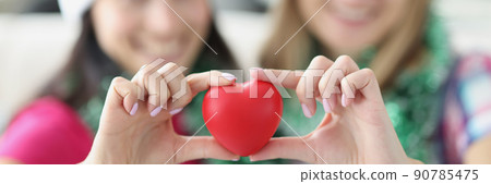 Sisters holding plastic red heart in hands and smiling Sisters holding plastic red heart in hands and smiling 90785475