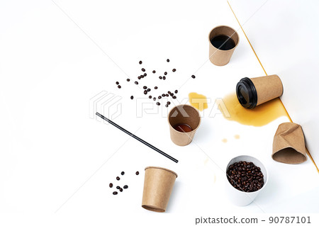 Disposable coffee cups, roasted coffee beans and spilling coffee on white table. Creative still life, copy space. 90787101
