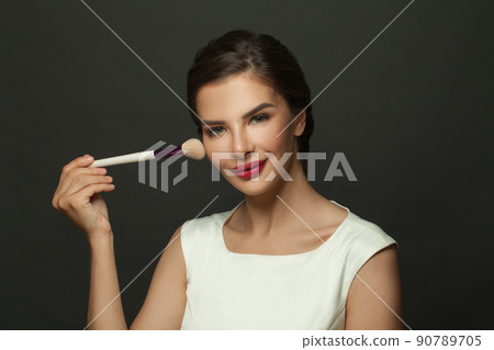 Close up beauty portrait of an attractive lovely young woman holding makeup blusher brush on black Close up beauty portrait of an attractive lovely young woman holding makeup blusher brush on black 90789705