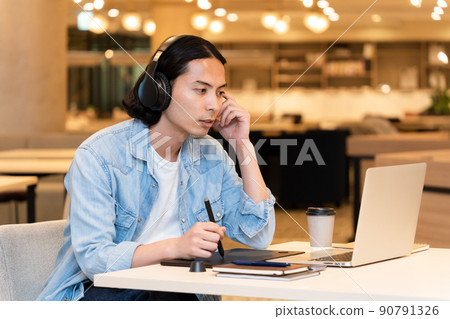A man wearing headphones and working on a pen tablet A man wearing headphones and working on a pen tablet 90791326