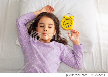 Cute brunette girl sleeps with a yellow alarm clock on a white pillow. 90792251