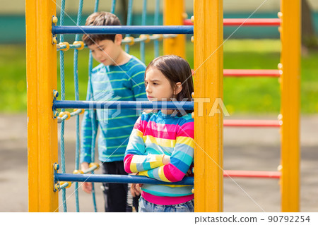 Sad and bored girl and boy stand among the yellow colorful playground, in the park Sad and bored girl and boy stand among the yellow colorful playground, in the park 90792254