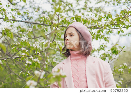 Portrait of little girl stands in a blooming white apple tree in the park. 90792260