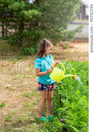 Little girl in a green T-shirt, watering a green bed of yellow watering can, in the garden Little girl in a green T-shirt, watering a green bed of yellow watering can, in the garden 90792299