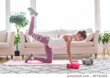 Sport and recreation concept. Young woman doing donkey kicks exercise indoor at home interior. 90792808