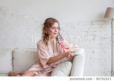 Pretty woman taking a bite of organic dark chocolate and cup of coffee indoor 90792823