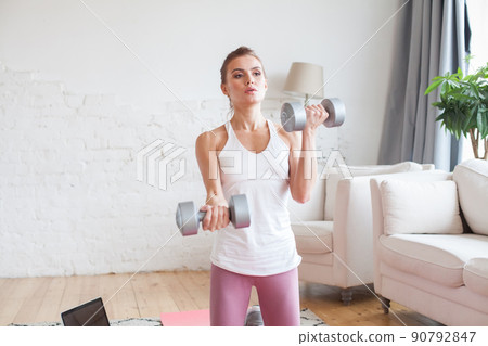 Strength sportswoman doing fitness exercises with dumbbells indoor.  90792847
