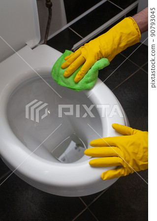 Hands of man in yellow gloves cleaning toilet bowl using cloth and detergent, concept  90793045