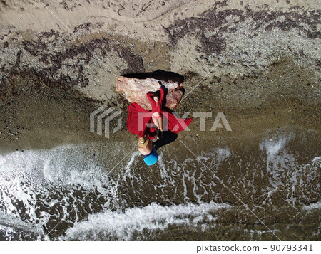 Top aerial view on a young sensual blonde woman in red bikini lying on the rock near water at sea and enjoys the sea waves. Dreams holidays and weekend vacation in summer time. Top aerial view on a young sensual blonde woman in red bikini lying on the rock near water at sea and enjoys the sea waves. Dreams holidays and weekend vacation in summer time. 90793341