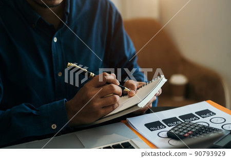 Male hand taking notes on a notebook handwritten note writing business schedule and use a laptop computer at the office desk. 90793929