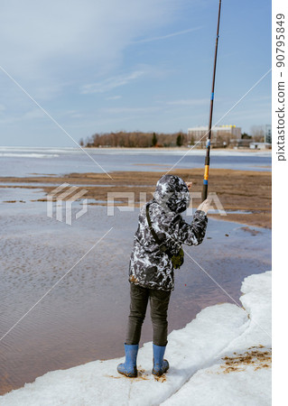 Cute little caucasian boy holding a fishing rod looking into distance on sea side on spring day 90795849
