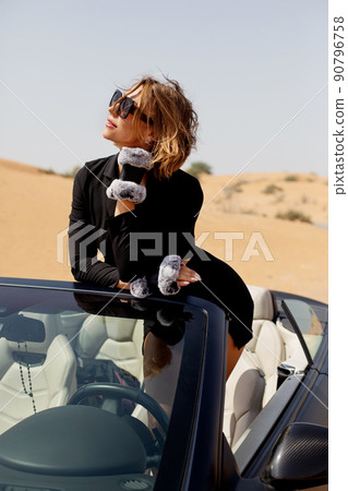Stylish young woman posing in a convertible car in the desert. Fashion, style, glamour Stylish young woman posing in a convertible car in the desert. Fashion, style, glamour 90796758