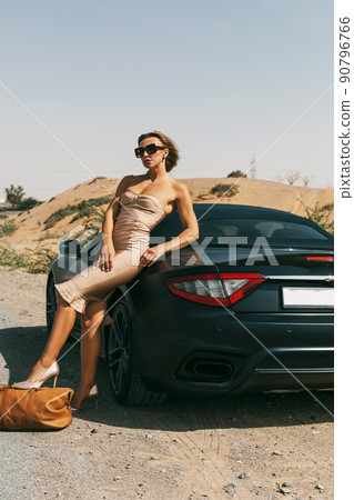 A beautiful sensual girl with blonde hair in an elegant dress posing in the desert near a car 90796766