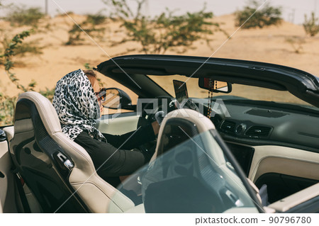 Glamorous blonde in a silk scarf and sunglasses in the driver's seat of a convertible convertible on a hot desert background. Fashion, style, glamour 90796780