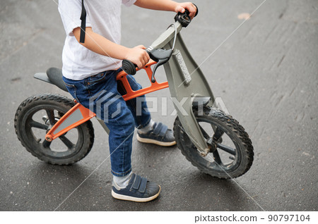 Cropped view of child holding bicycle handlebar while riding balance bike outdoors. 90797104