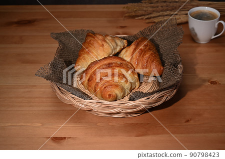 Freshly baked croissants in wicker basket and coffee cup on wooden tale. Breakfast, bread bakery products cafe concept 90798423