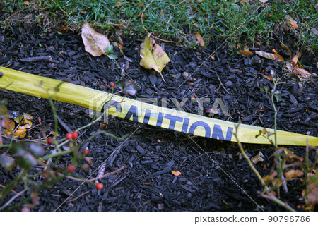 The yellow Caution tape laying on the ground with the soil and the grass 90798786