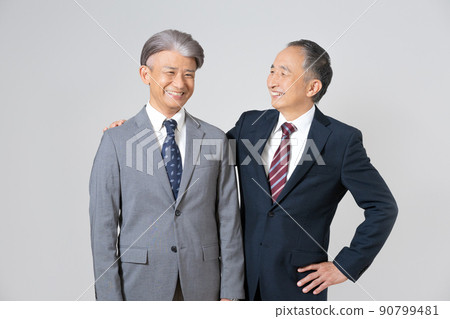 Two senior men wearing suits, crossing their shoulders and putting their hands on their hips Two senior men wearing suits, crossing their shoulders and putting their hands on their hips 90799481