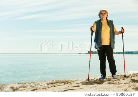 Senior woman practicing nordic walking on beach Senior woman practicing nordic walking on beach 90800187