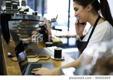 Smiling waitress talking on cellular with clients reserving table in coffee shop 90800969