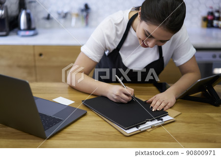 Skilled woman barista filling in invoice concentrated on numbers Skilled woman barista filling in invoice concentrated on numbers 90800971