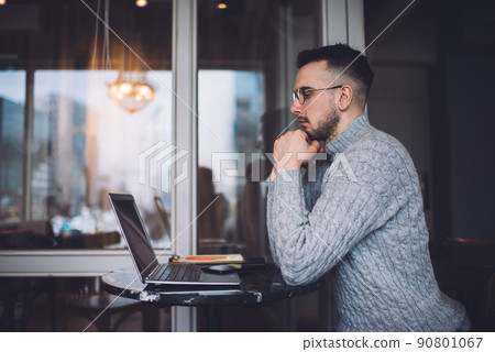 Thoughtful young man working on laptop in contemporary workplace 90801067