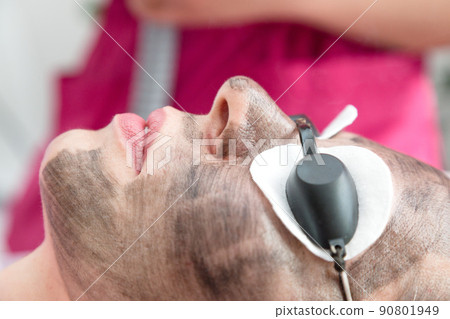 Woman patient taking carbon peel procedure on face 90801949