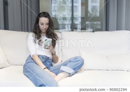 Young european woman using smartphone in home relaxed environment on sofa in free time. Internet, technology concept. 90802294