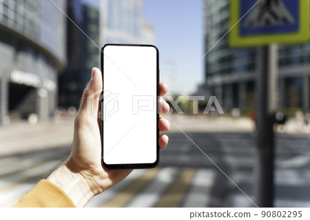 A smartphone in a hand with a blank screen against the backdrop of an urban street of the business quarter of the city. Business applications, transport, taxi, maps concept 90802295