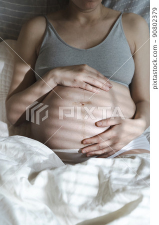 A pregnant woman strokes her belly with a baby before childbirth while relaxing in a sunny bright bedroom lying on a bed. Women's health, pregnancy, conception, childbirth concept. A pregnant woman strokes her belly with a baby before childbirth while relaxing in a sunny bright bedroom lying on a bed. Women's health, pregnancy, conception, childbirth concept. 90802379