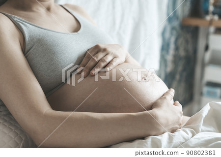 A pregnant woman strokes her belly with a baby before childbirth while relaxing in a sunny bright bedroom lying on a bed. Women's health, pregnancy, conception, childbirth concept. A pregnant woman strokes her belly with a baby before childbirth while relaxing in a sunny bright bedroom lying on a bed. Women's health, pregnancy, conception, childbirth concept. 90802381