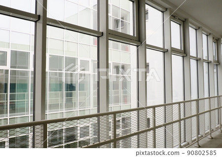 New double-glazed windows and glass windows in the school. View from the window to the opposite wall and windows. Silhouettes of people behind glass. New white building. New double-glazed windows and glass windows in the school. View from the window to the opposite wall and windows. Silhouettes of people behind glass. New white building. 90802585