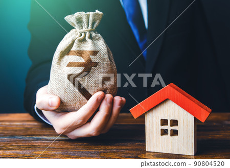 Man holds out a indian rupee bag near the house. Property appraisal. Favorable terms and conditions, low interest rate. Bank approval for issuing a mortgage loan. Home purchase, invest in real estate. 90804520