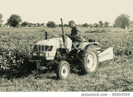 A farmer on a tractor is working on a farm field. Agroindustry and agribusiness. Agricultural sector of the economy. Plant food production. Machinery and equipment. 90804569
