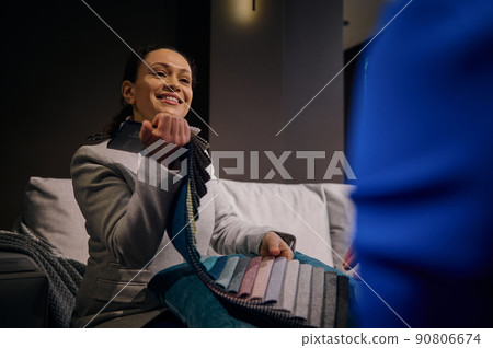 Pleasant female interior designer helps customer with their home restoration design project, demonstrates a large palette with upholstery fabric samples. Interior and home design concept 90806674