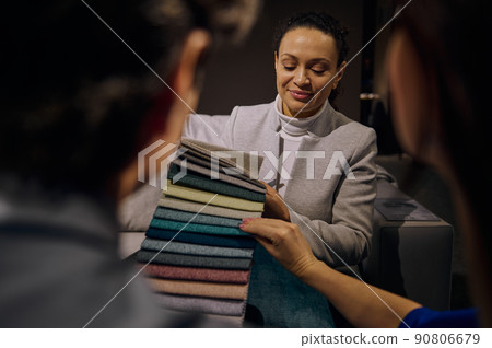 Confident clerk in interior design showroom showing to customers fabric samples for sofa restoration and upholstery. Home improvement and renovation Confident clerk in interior design showroom showing to customers fabric samples for sofa restoration and upholstery. Home improvement and renovation 90806679