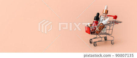 Online shopping minimalistic concept. Small cart with cosmetic bottles. Essential oil, serum and peeling gel in glass droppers. Mixture of beauty products. Online shopping minimalistic concept. Small cart with cosmetic bottles. Essential oil, serum and peeling gel in glass droppers. Mixture of beauty products. 90807135