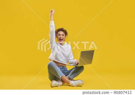 Excited woman celebrating victory, looking at netbook screen inside. Front view of happy female freelancer enjoying successful startup, raising hand, isolated on orange background. Concept of emotion. Excited woman celebrating victory, looking at netbook screen inside. Front view of happy female freelancer enjoying successful startup, raising hand, isolated on orange background. Concept of emotion. 90807412
